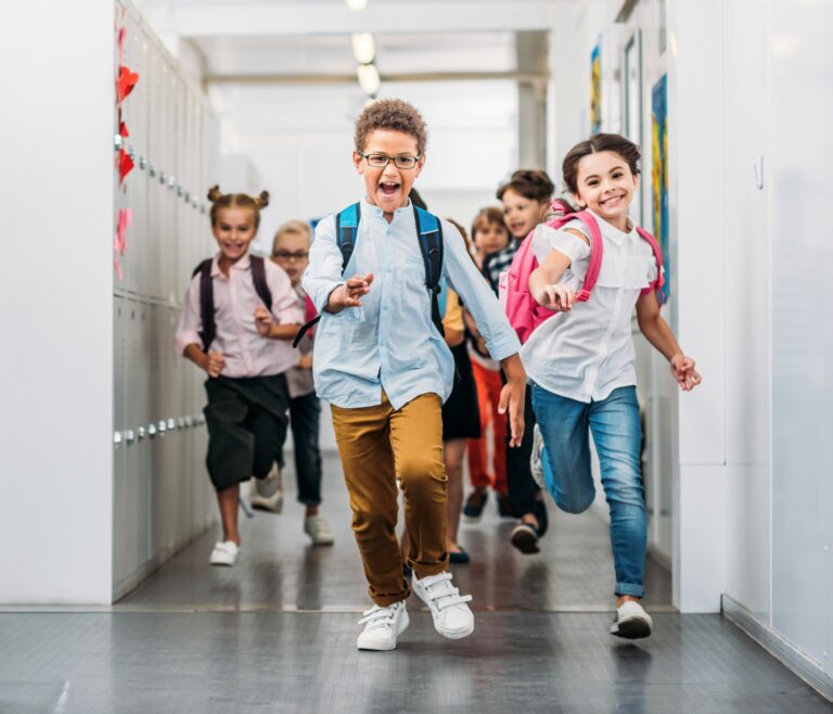 De jeunes enfants portant des sacs à dos courent avec enthousiasme dans le couloir de l’école. Des casiers tapissent les murs