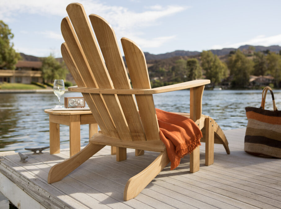 Chaise Muskoka en bois naturel sur un quai drapé d’une couverture orange, un verre de vin et un haut-parleur portable reposent juste à côté sur une petite table