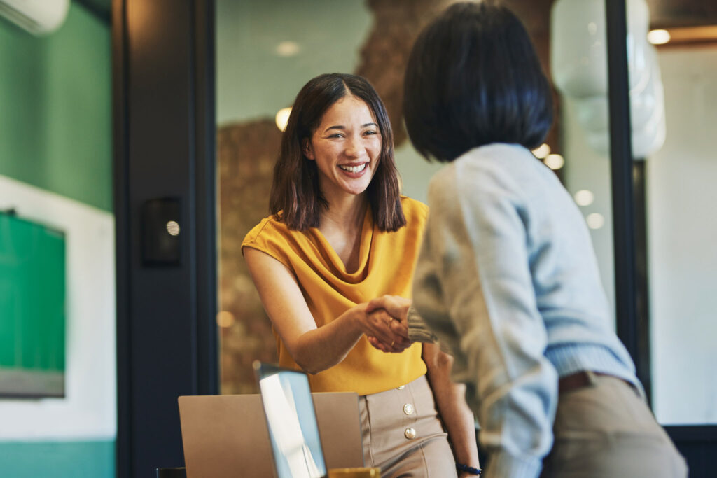 Une jeune femme serre la main d'une autre femme vêtue d'une tenue professionnelle.