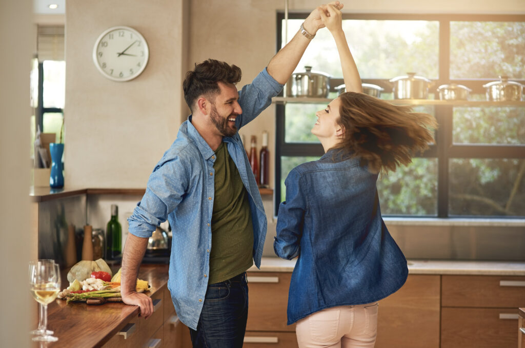 Jeune couple heureux dansant dans la cuisine; la lumière chaude du soleil pénètre par la fenêtre