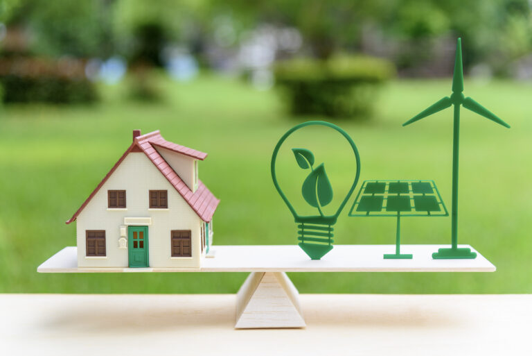 Maison jouet sur une balançoire équilibrée par une ampoule écoénergétique jouet, un panneau solaire et une éolienne