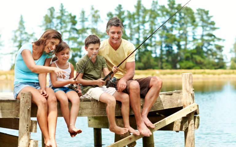Mère et père assis sur un quai avec leur fille et leur fils qui pêchent, souriants