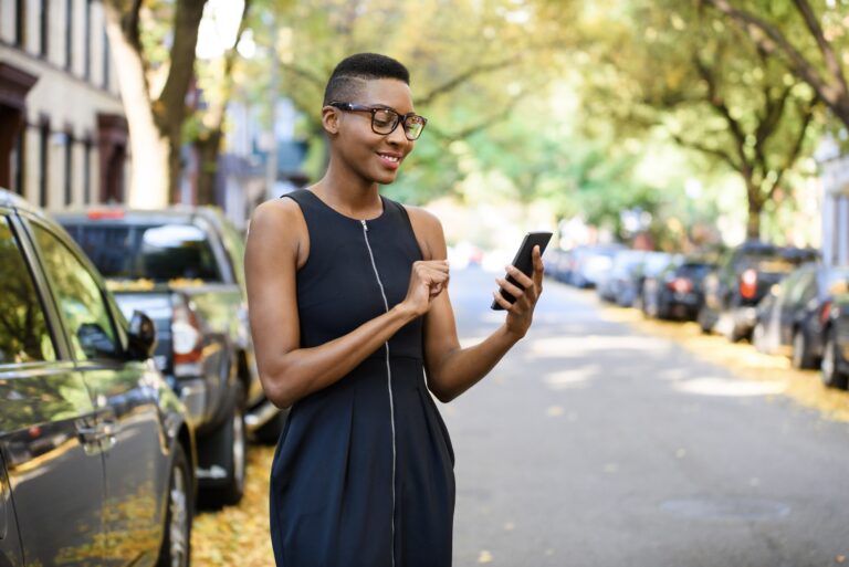 Jeune femme en ville utilisant son téléphone cellulaire pour rechercher une propriété