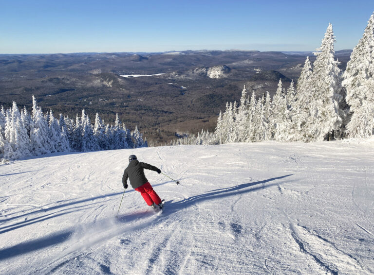 Skieur portant des pantalons de neige rouge au sommet d’une montagne, amorçant sa descente