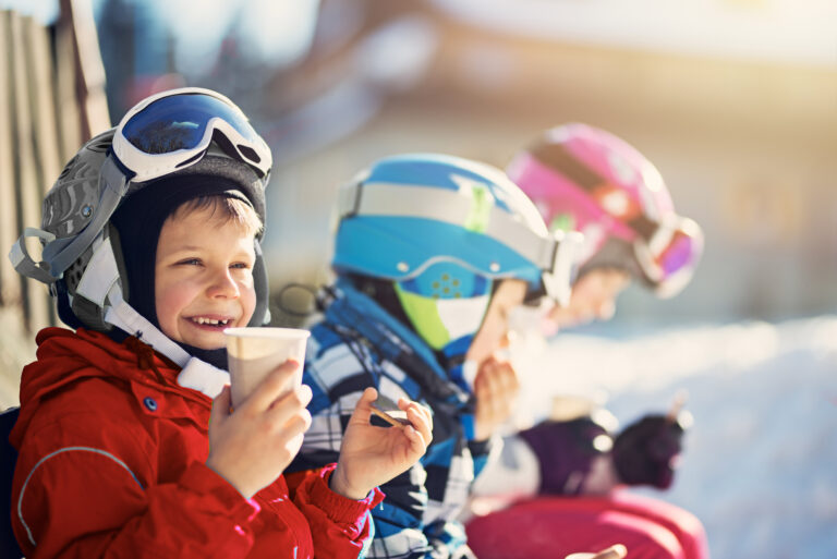 Jeunes enfants au pied d’un mont de ski buvant du chocolat chaud