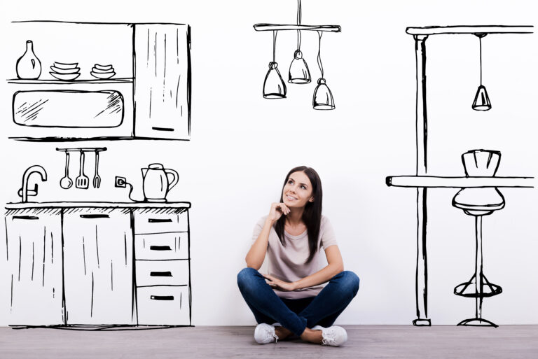 Une jeune femme assise sur le plancher d’une pièce s’imagine à quoi ressemblera sa nouvelle cuisine