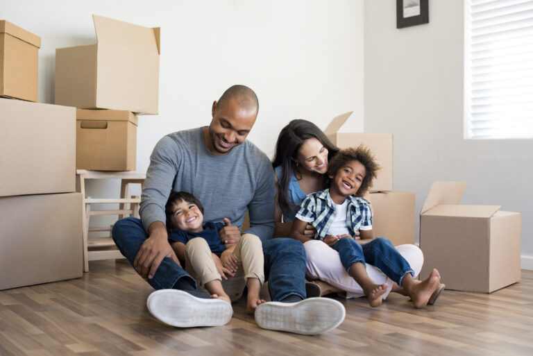 Un jeune couple avec deux fils est assis par terre devant des cartons de déménagement.