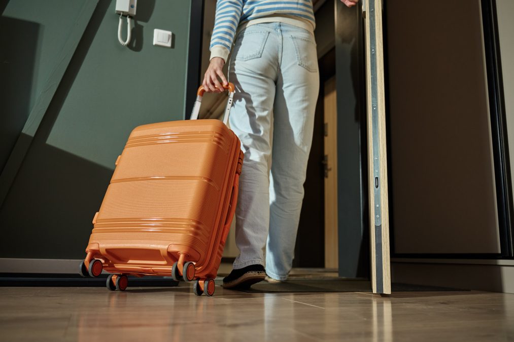 Une femme sort de l'appartement avec une valise orange