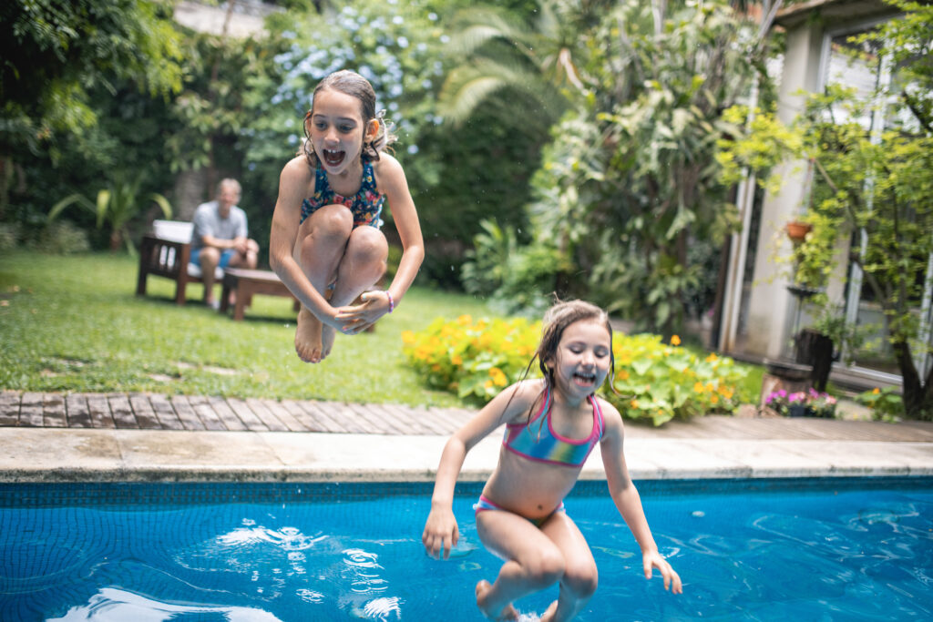 Deux jeunes enfants sautent dans une piscine de cour arrière, et ils sourient, rient et s’amusent