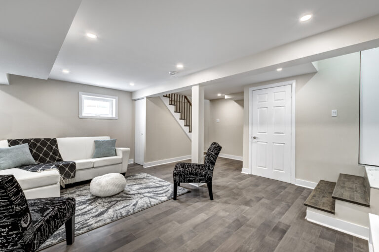 Sous-sol moderne et rénové avec des planchers de bois franc gris, un canapé blanc et des chaises d'appoint noires