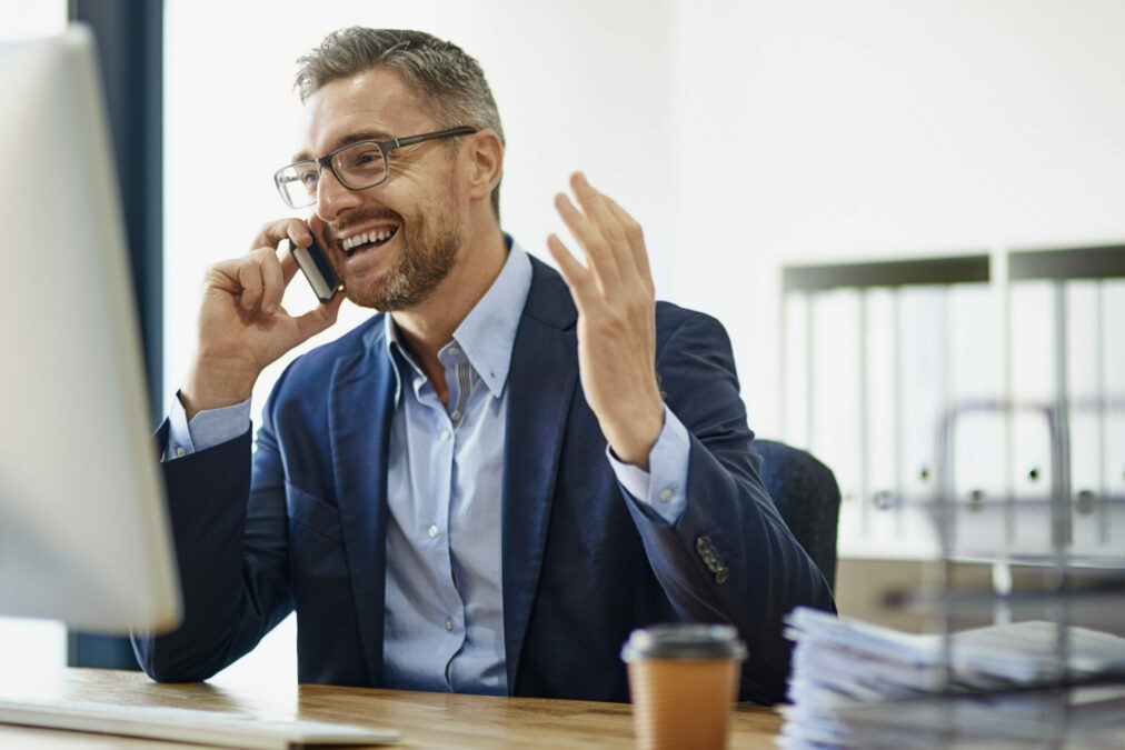 Happy businessman and successful real estate investor using his phone and computer at his desk