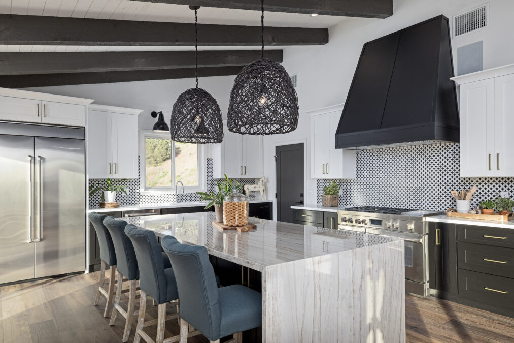 Intérieur d'une cuisine de luxe moderne et sombre avec un îlot en marbre en forme de cascade, des tabourets de bar bleus et des lampes suspendues noires tissées