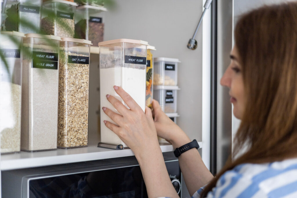 Une femme dépose un contenant alimentaire étiqueté dans une armoire de cuisine.