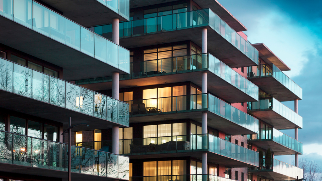 Édifice moderne d’appartements en copropriété aux balcons de verre, sous un ciel sombre et ennuagé