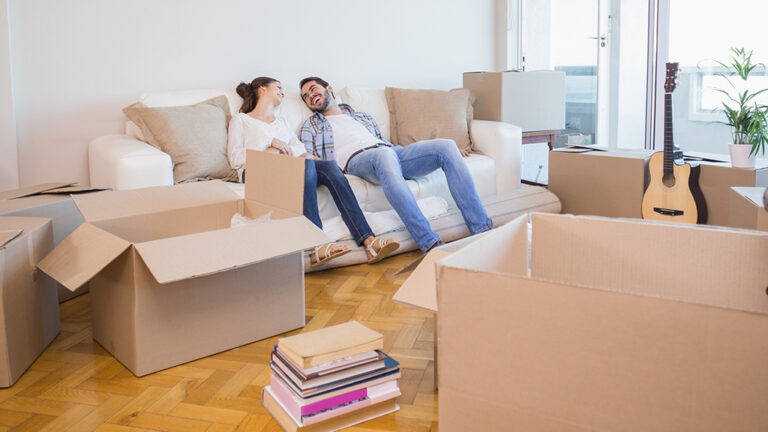 Un jeune couple assis sur un sofa dans un appartement moderne entouré de boîtes de déménagement