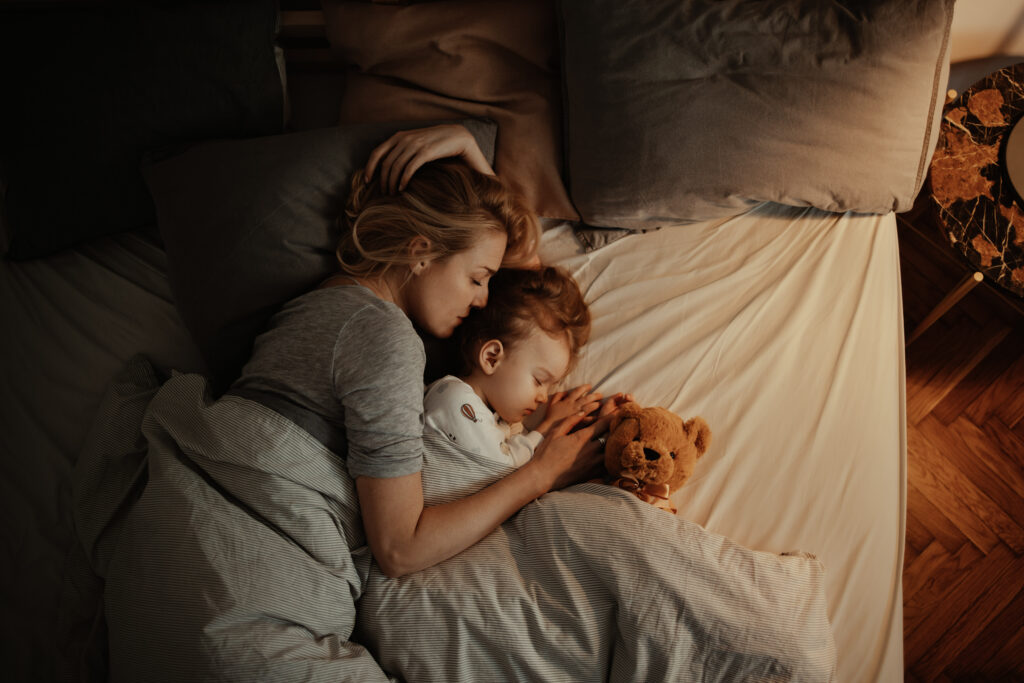 Une mère et sa fille endormies sur un lit où se trouve également un ours en peluche