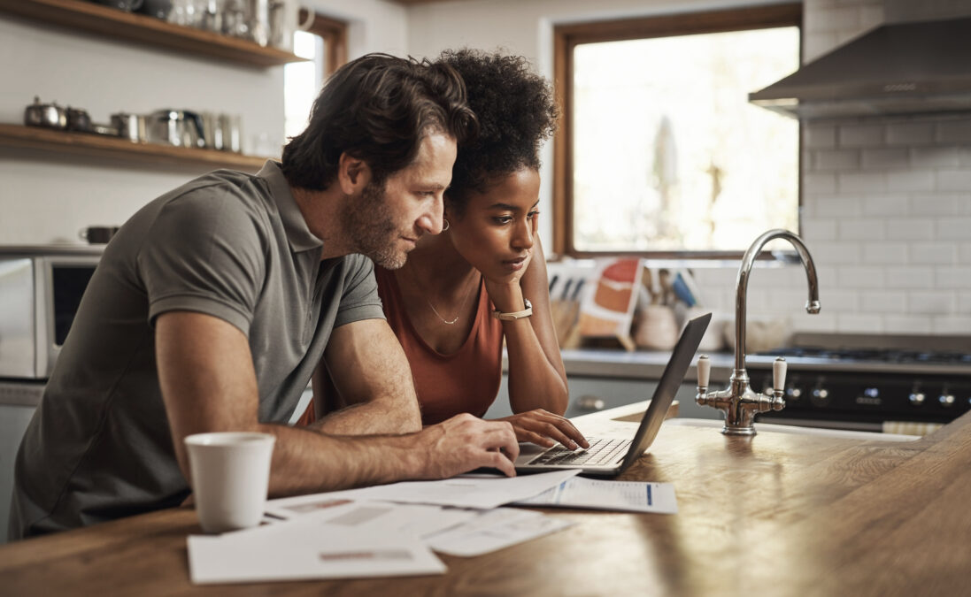 Un couple devant leur ordinateur portable feuillant des documents sur l'îlot de la cuisine