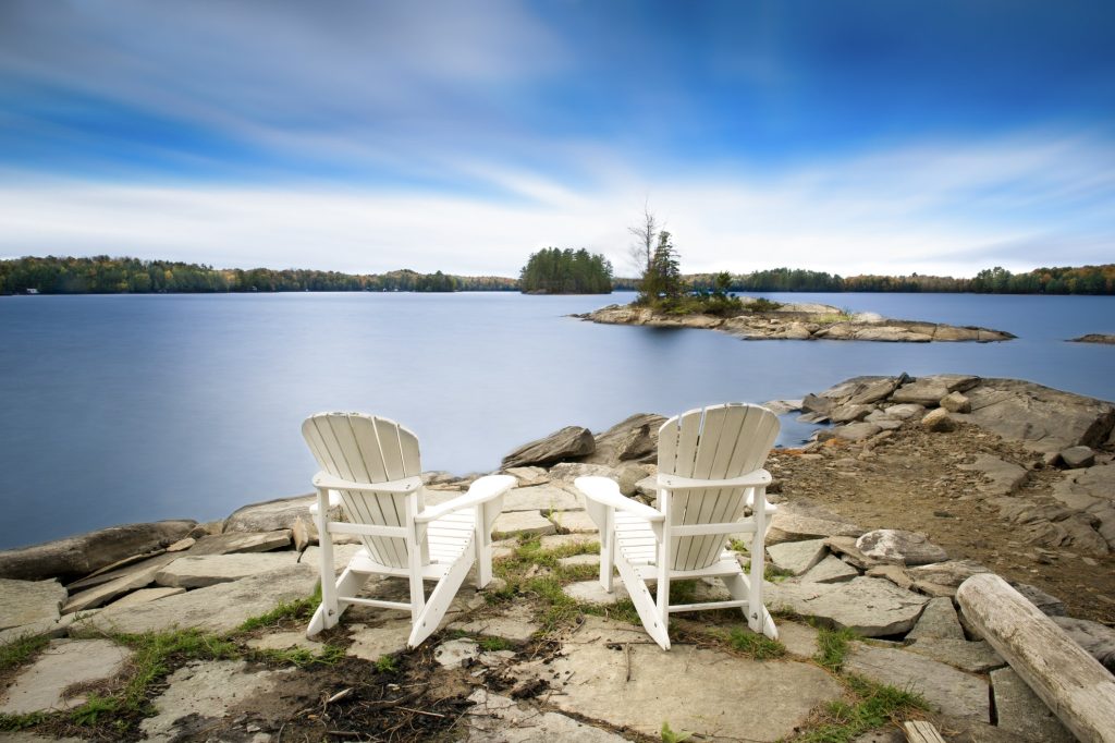 Deux fauteuils blancs de style Muskoka sur des roches surplombant l’eau