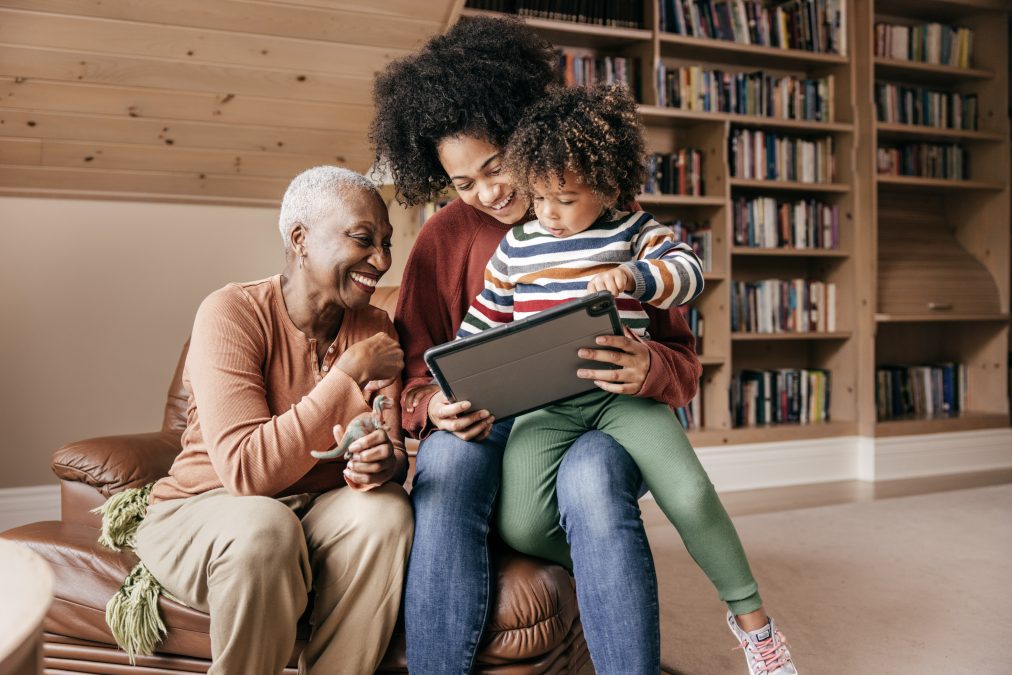 Une femme, sa mère et son enfant sont assis et regardent quelque chose ensemble sur une tablette dans une bibliothèque