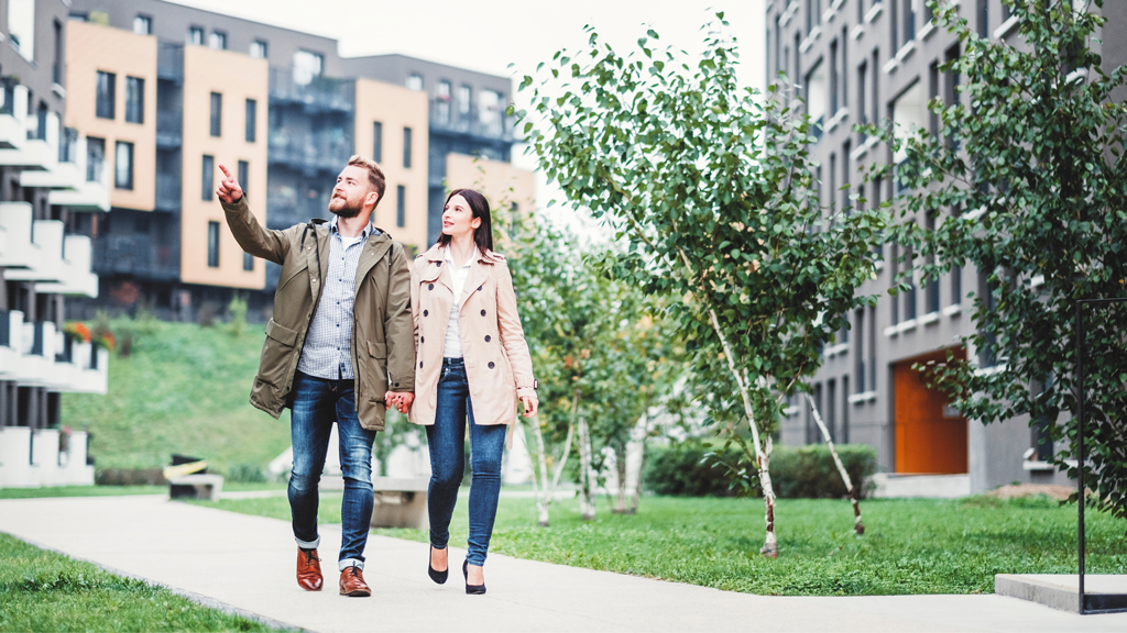 Un jeune couple marche dans un chemin se tenant par la main en regardant les immeubles de condos modernes