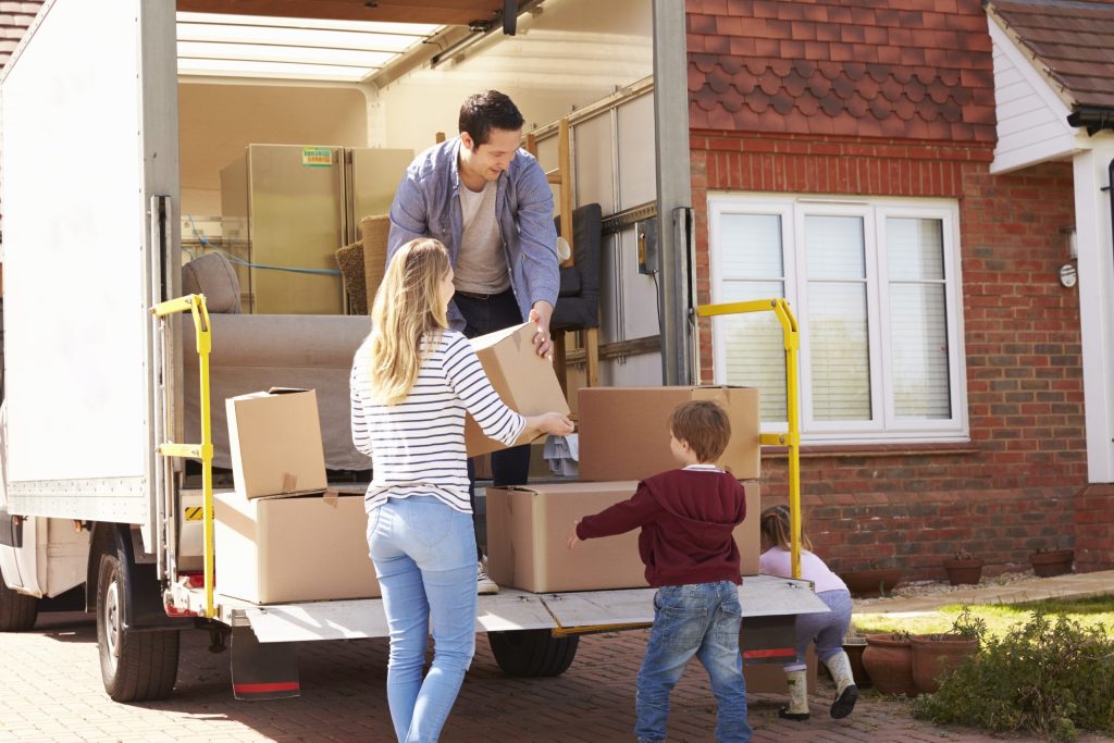 Une jeune famille avec des enfants qui décharge des boîtes d’un camion de déménagement pour les amener dans leur nouvelle résidence