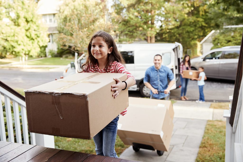 Une jeune fille porte une boîte de déménagement sur les marches d’entrée d’une maison