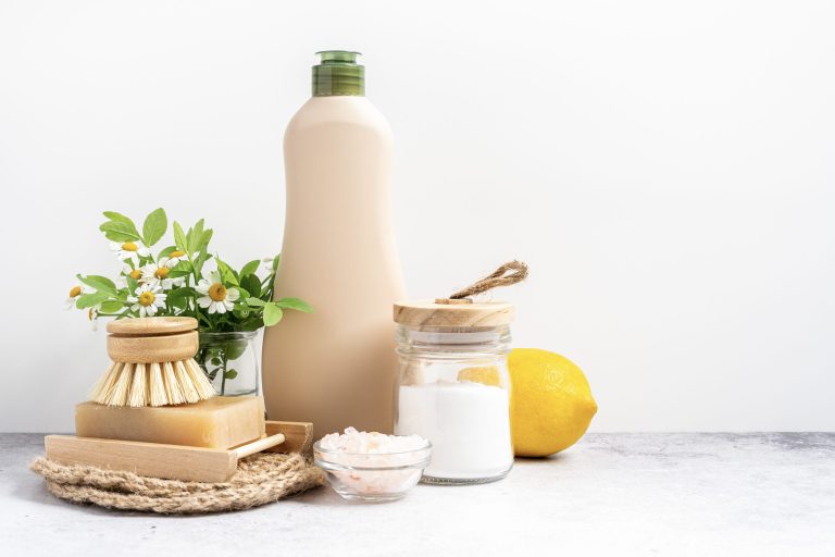 Nettoyants naturels écologiques, bocal avec bicarbonate de soude, brosse à vaisselle, citron, fleurs, savon sur fond blanc.