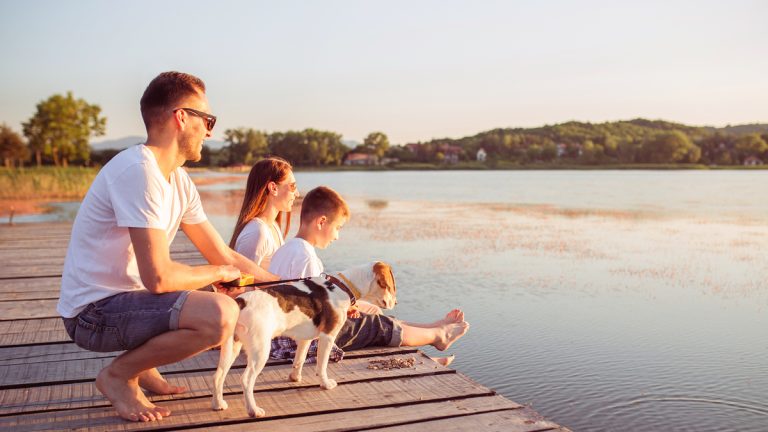Famille et chien assis sur un quai au bord d'un lac pendant le coucher du soleil.
