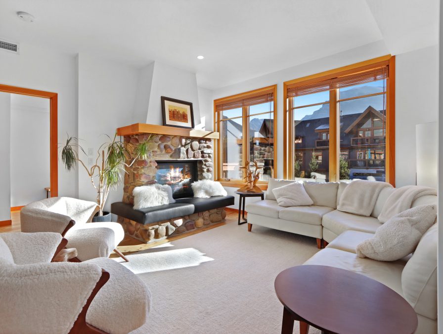 Un salon d'appartement ensoleillé avec une cheminée en pierre donnant sur les montagnes Rocheuses.