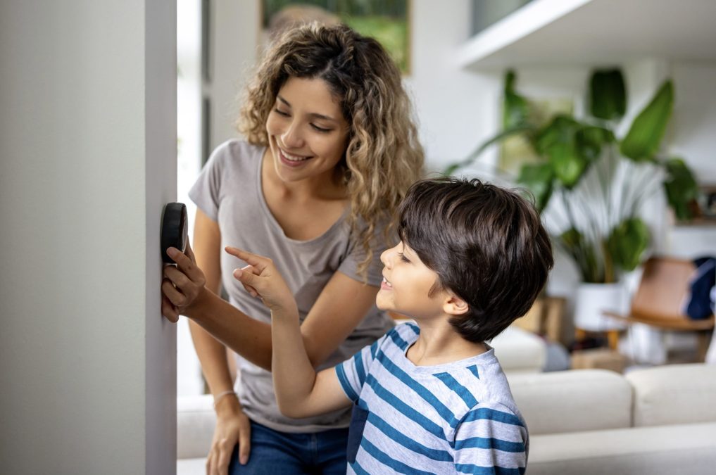 Mère et fils heureux à la maison utilisant un thermostat intelligent pour ajuster la température