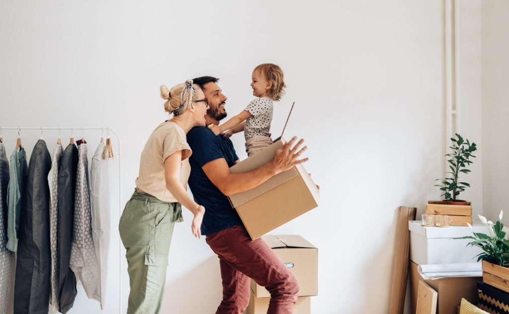 Une famille heureuse avec un enfant s'amusant à porter et à déballer des cartons dans sa nouvelle maison le jour du déménagement.