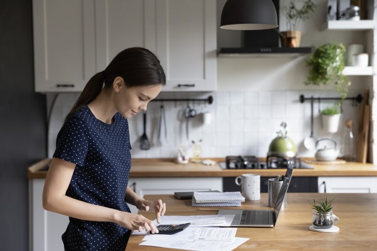 Woman uses calculator and laptop at kitchen island