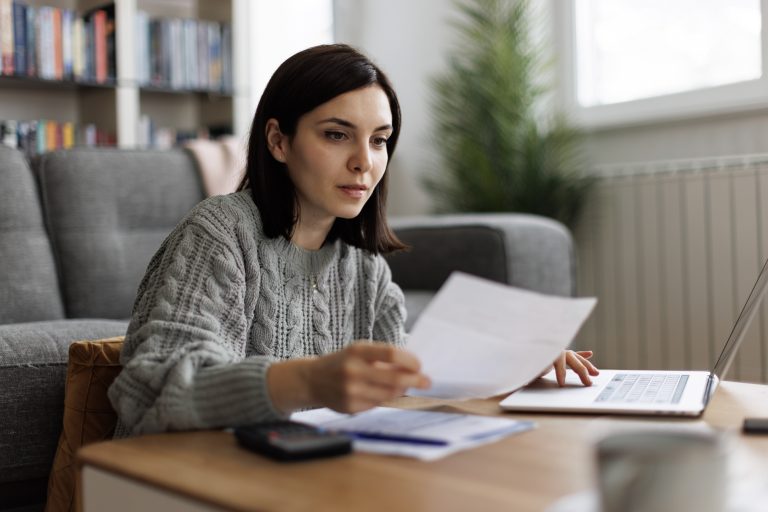 Une femme en pull gris lisant des documents financiers sur une table basse.