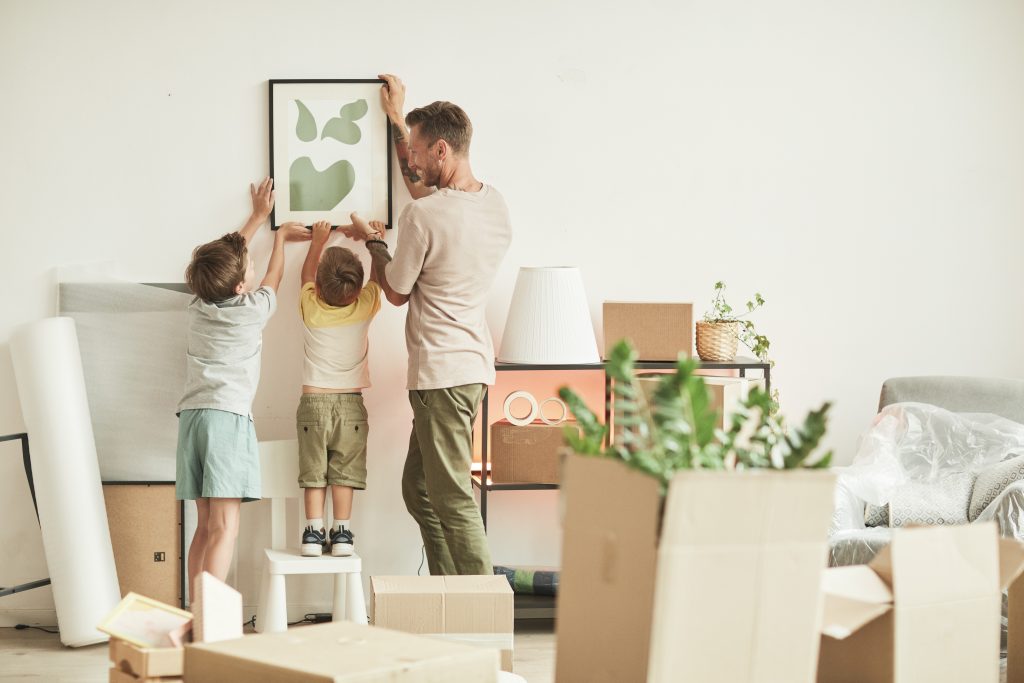 Un père et ses deux jeunes fils accrochent une photo encadrée sur un mur