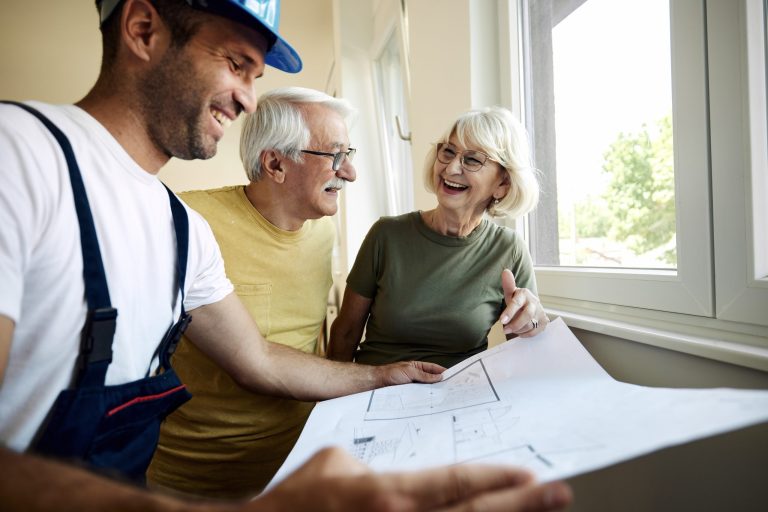 Couple d'âge mûr heureux examinant des plans avec un ouvrier lors de la rénovation d'une maison
