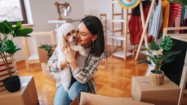 Une jeune femme tenant un petit chien blanc entouré de cartons de déménagement