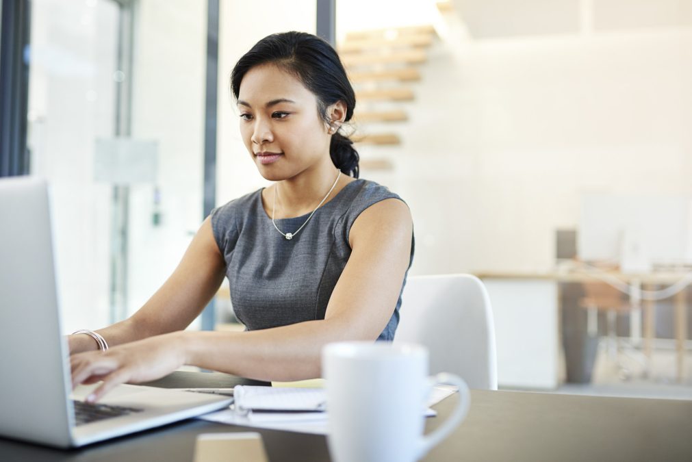 Une jeune femme en tenue de travail tape sur un ordinateur portable à un bureau