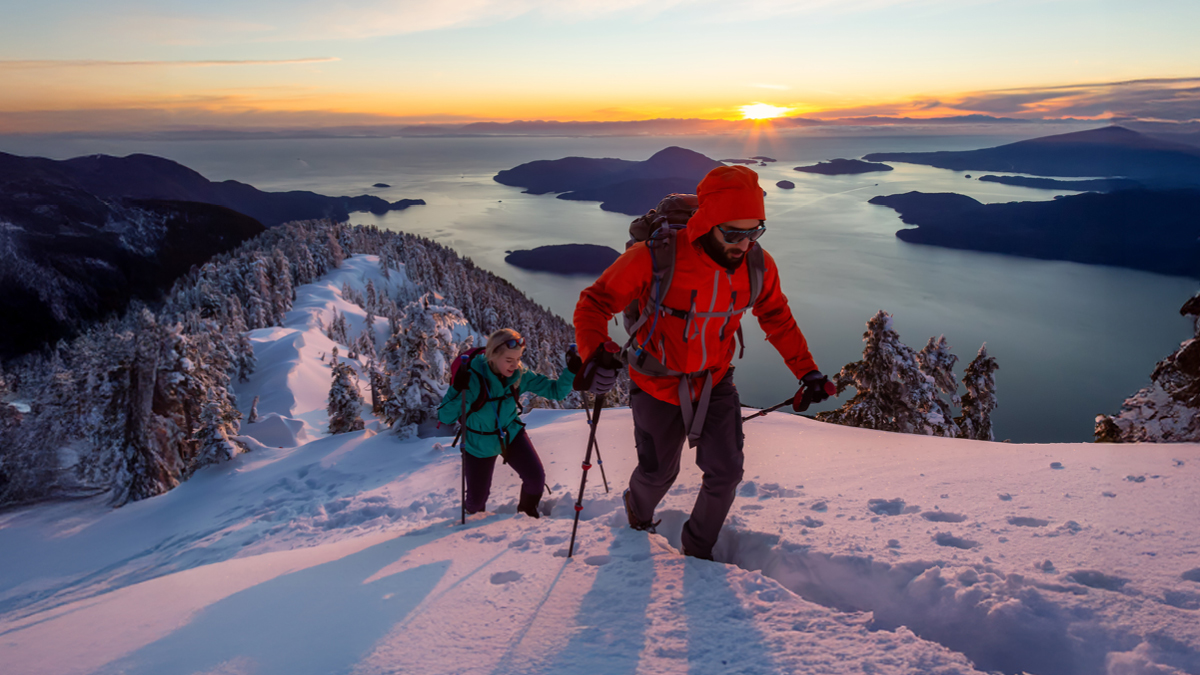 Un homme et une femme font de la randonnée au sommet d'une montagne pendant un coucher de soleil hivernal éclatant.