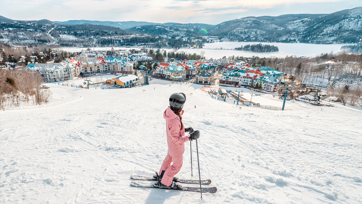Une skieuse vêtue d'une combinaison rose au sommet d'une piste de ski contemple la ville colorée en contrebas