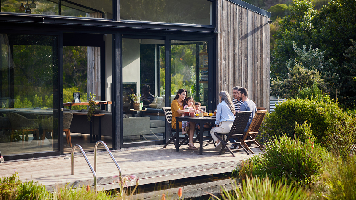Une famille multigénérationnelle dîne autour d’une table sur une terrasse extérieure en été.