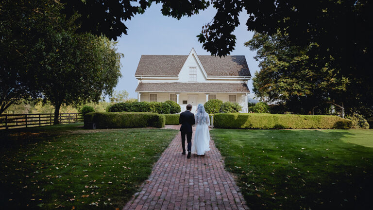 Les mariés le jour de leur mariage, debout devant une maison blanche par une journée d’été
