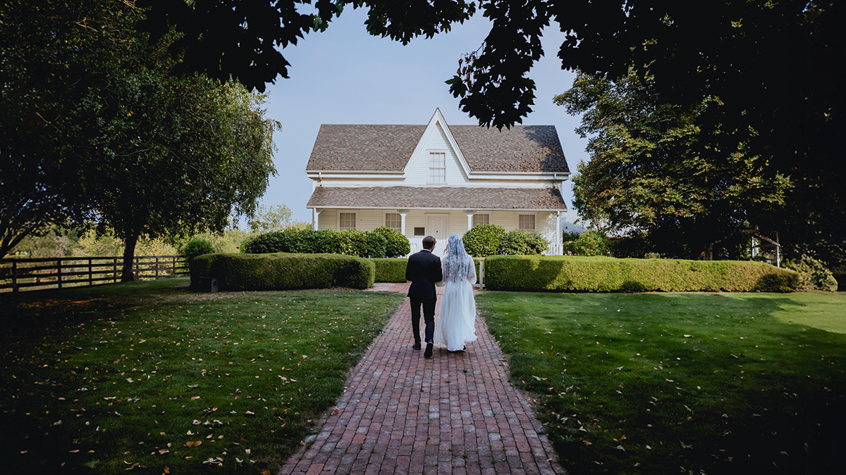 Les mariés le jour de leur mariage, debout devant une maison blanche par une journée d’été
