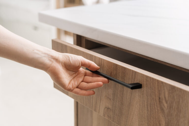 Gros plan d’une main de femme ouvrant un tiroir en bois dans une cuisine contemporaine au design épuré et minimaliste.