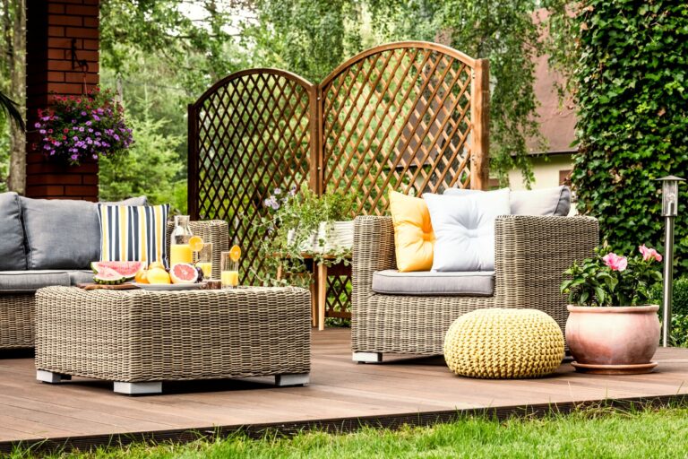 Jus de pamplemousse et d'orange sur une table, sur une terrasse en bois, avec un pouf jaune à côté d'un fauteuil.