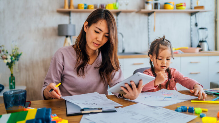 Une jeune mère examine ses comptes, tandis que sa fille est assise à côté d'elle et joue.
