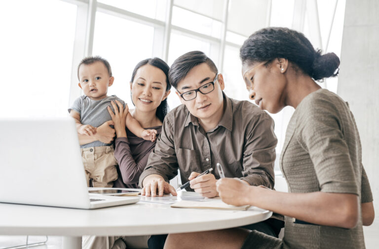 Une jeune famille avec un bébé consulte un courtier en prêts immobiliers autour d'une table.