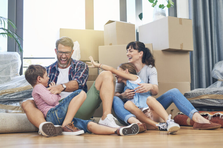 Une famille assise par terre chez elle, devant des cartons de déménagement