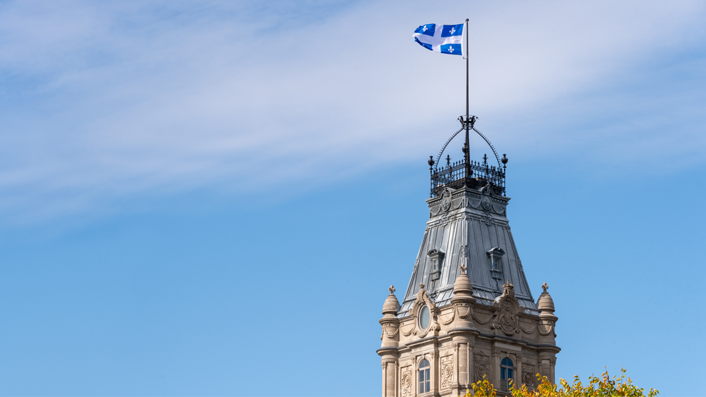 Vue extérieure du sommet du parlement provincial du Québec; le drapeau du Québec flotte au soleil.