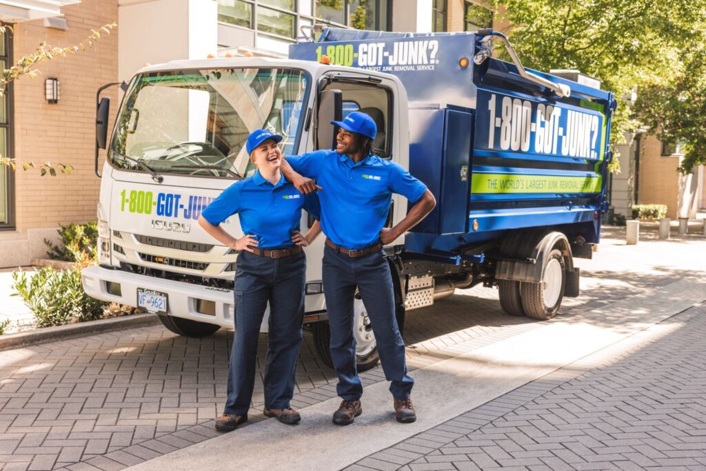 Deux membres souriants de l'équipe 1-800-GOT-JUNK?, vêtus d'uniformes bleus, debout devant un camion d'enlèvement de déchets à l'effigie de l'entreprise.