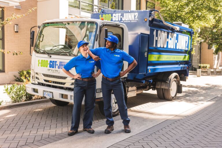 Deux membres souriants de l'équipe 1-800-GOT-JUNK?, vêtus d'uniformes bleus, debout devant un camion d'enlèvement de déchets à l'effigie de l'entreprise.
